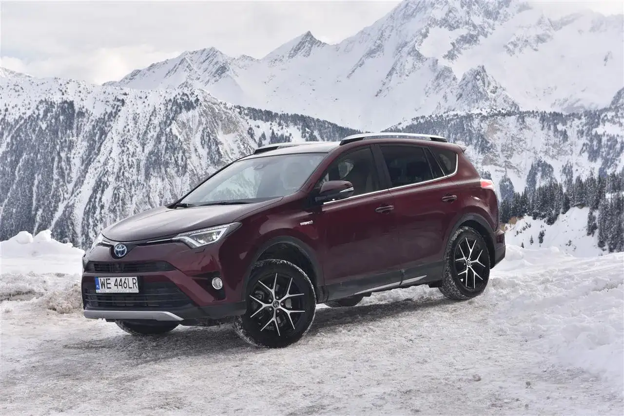 Ciemnoczerwona Toyota RAV4 Hybrid na tle ośnieżonych gór. Zastanawiasz się, ile przejedzie hybryda Toyoty w takich warunkach?