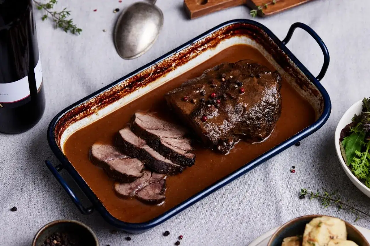 Ein köstliches Rehschulter Rezept: zartes Fleisch in dunkler Sauce, garniert mit Pfefferkörnern, serviert mit Beilagen.