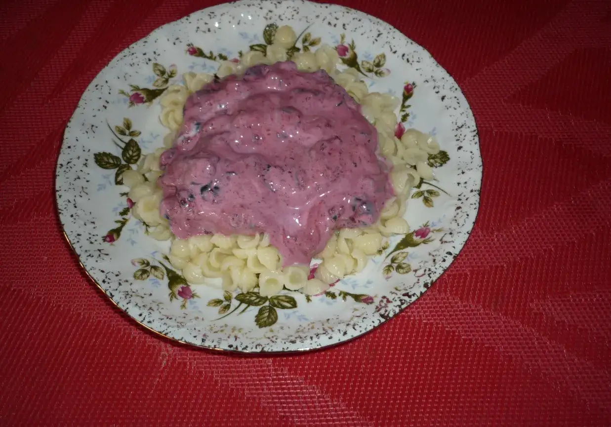 Makaron z jagodami w kremowym sosie, podany na ozdobnym talerzu.