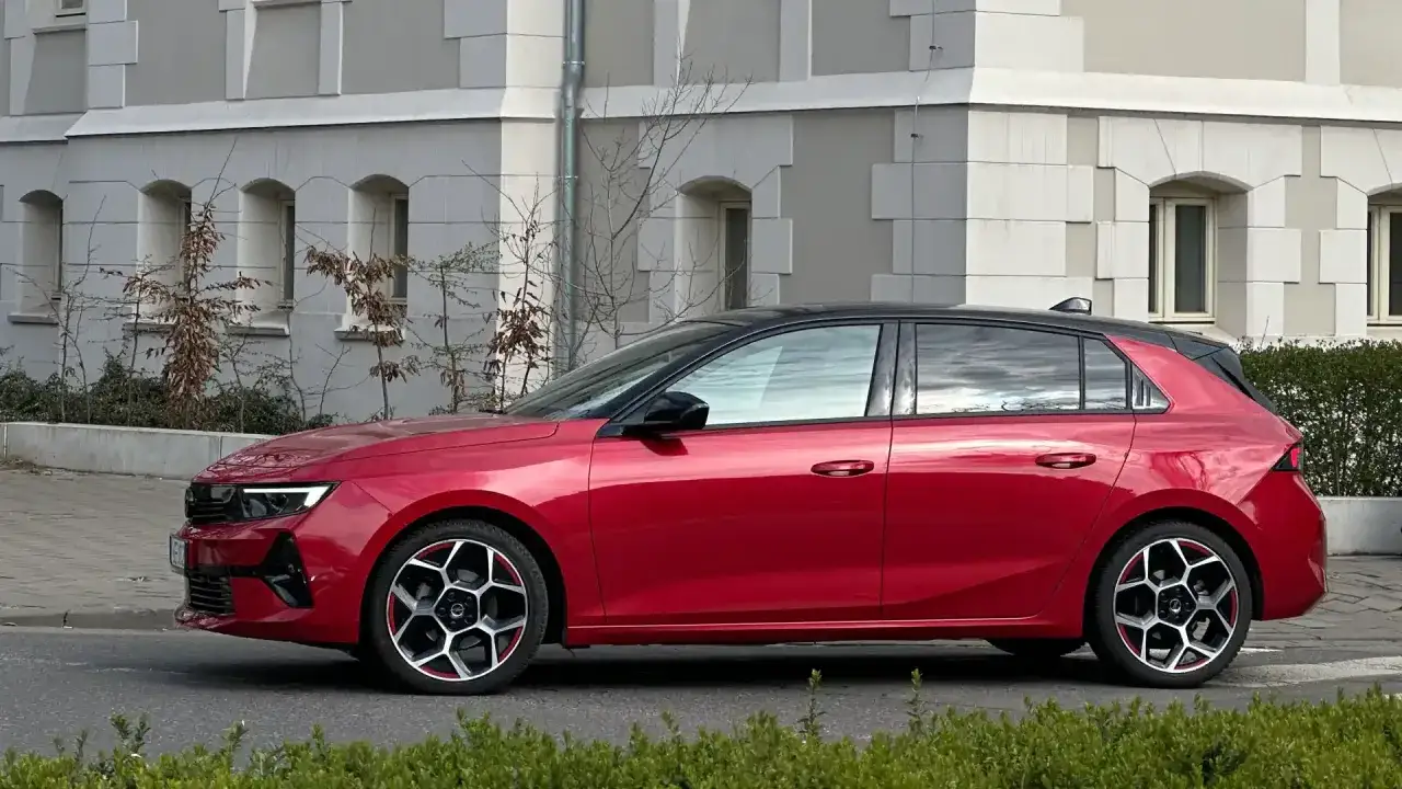 Czerwony Opel Astra Turbo z czarnym dachem i efektownymi felgami stoi przed budynkiem z arkadowymi oknami.
