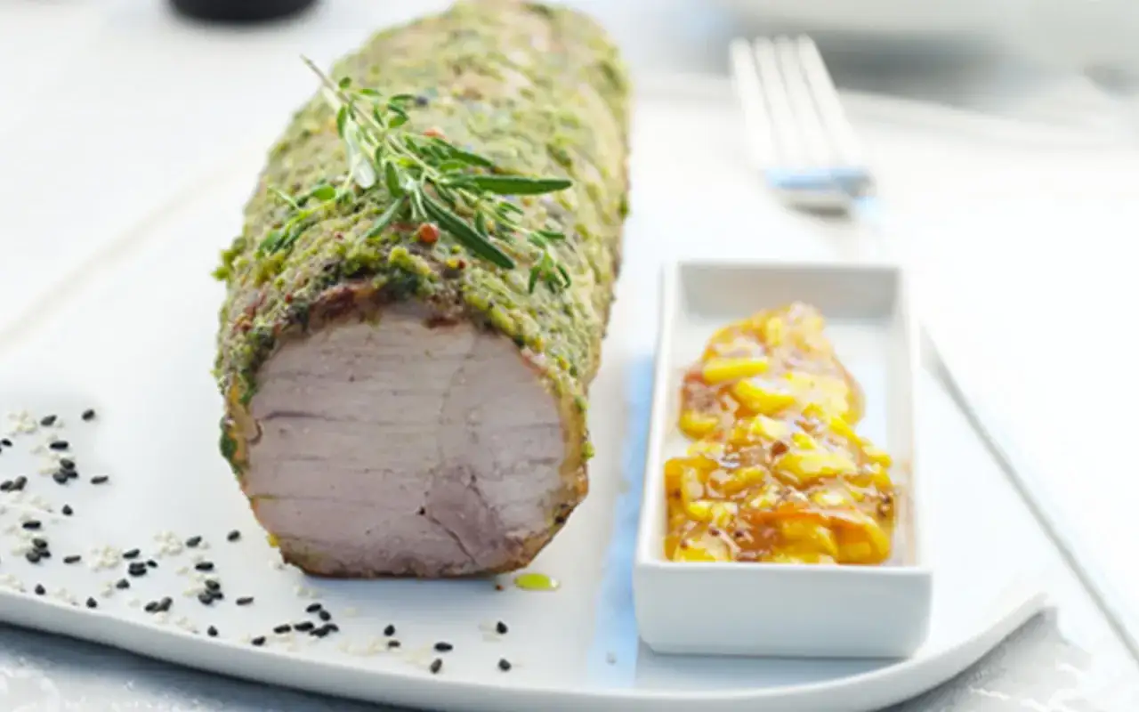 Filet mignon en croûte d'herbes, prêt pour la cuisson, servi avec une compotée de fruits et des graines de sésame.