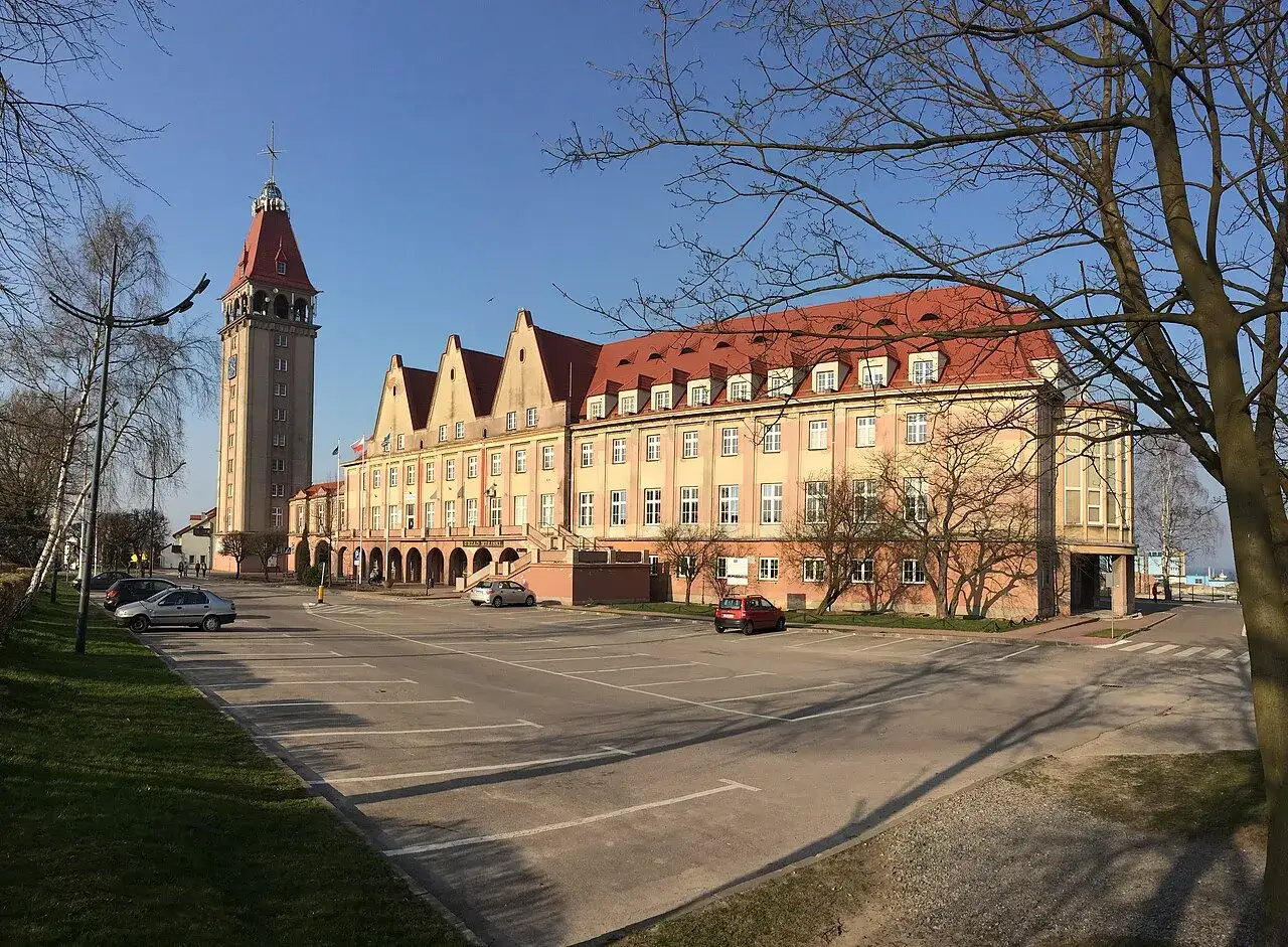 Dawny dom rybaka z charakterystyczną wieżą i czerwonym dachem, otoczony parkingiem i drzewami.