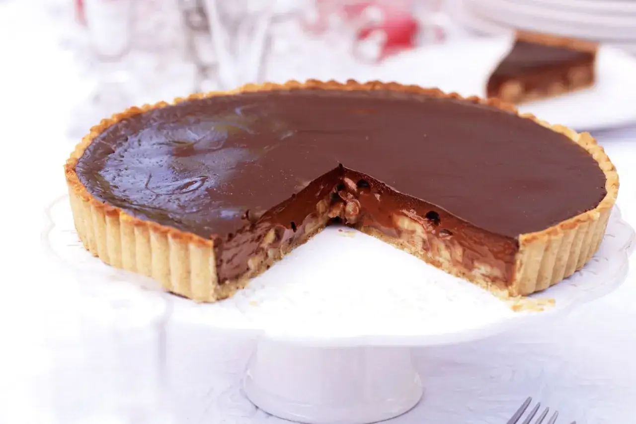 Tarte banane chocolat on un plateau blanc, une part coup&eacute;e r&eacute;v&egrave;le la garniture cr&eacute;meuse et les rondelles de banane.