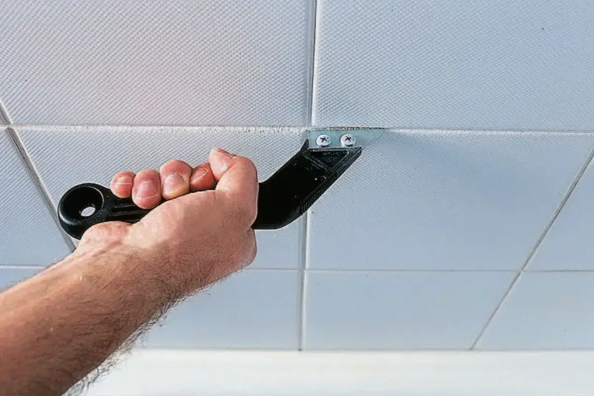 Hand uses a tool to remove old silicone from tiled surfaces, preparing for silikon risse ausbessern.