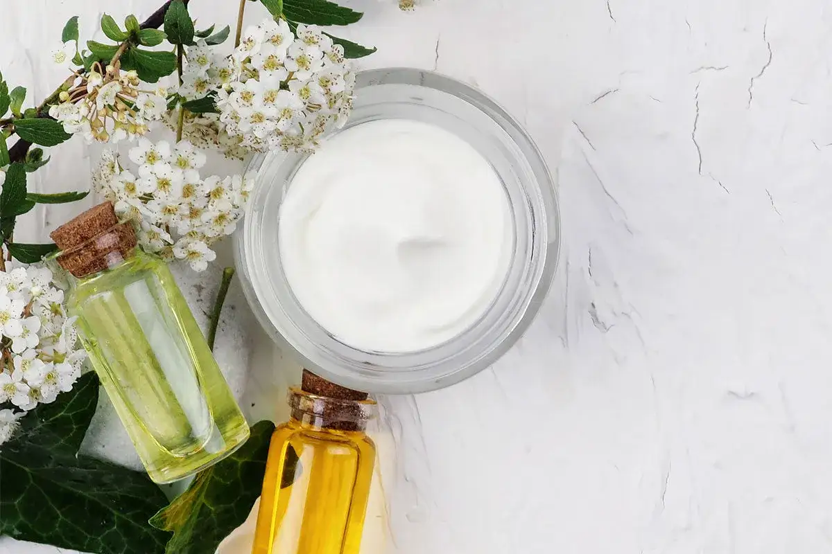 Krem w słoiczku, buteleczki z olejkami i białe kwiaty. Składniki, jak caprylic capric triglyceride, tworzą naturalne kosmetyki.