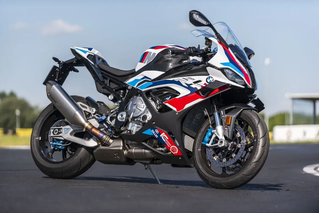 Sportowy motocykl BMW M1000RR w barwach M, z karbonowymi elementami i wydechem Akrapovič, gotowy do wyścigu.