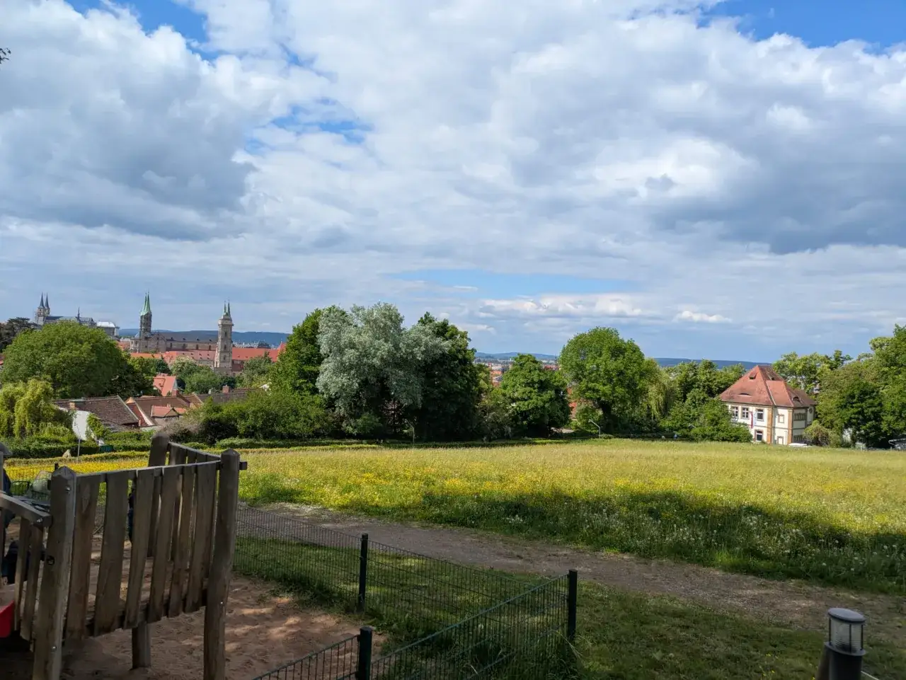 Blick &uuml;ber eine Blumenwiese auf Bamberg mit seinen T&uuml;rmen. Ein Spielplatz im Vordergrund, perfekt f&uuml;r Entdeckungen abseits der Touristenpfade &ndash; echte Bamberg Geheimtipps.