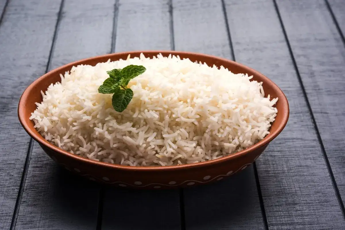 Parująca miska ryżu basmati ig, ozdobiona listkiem mięty, na drewnianym blacie.