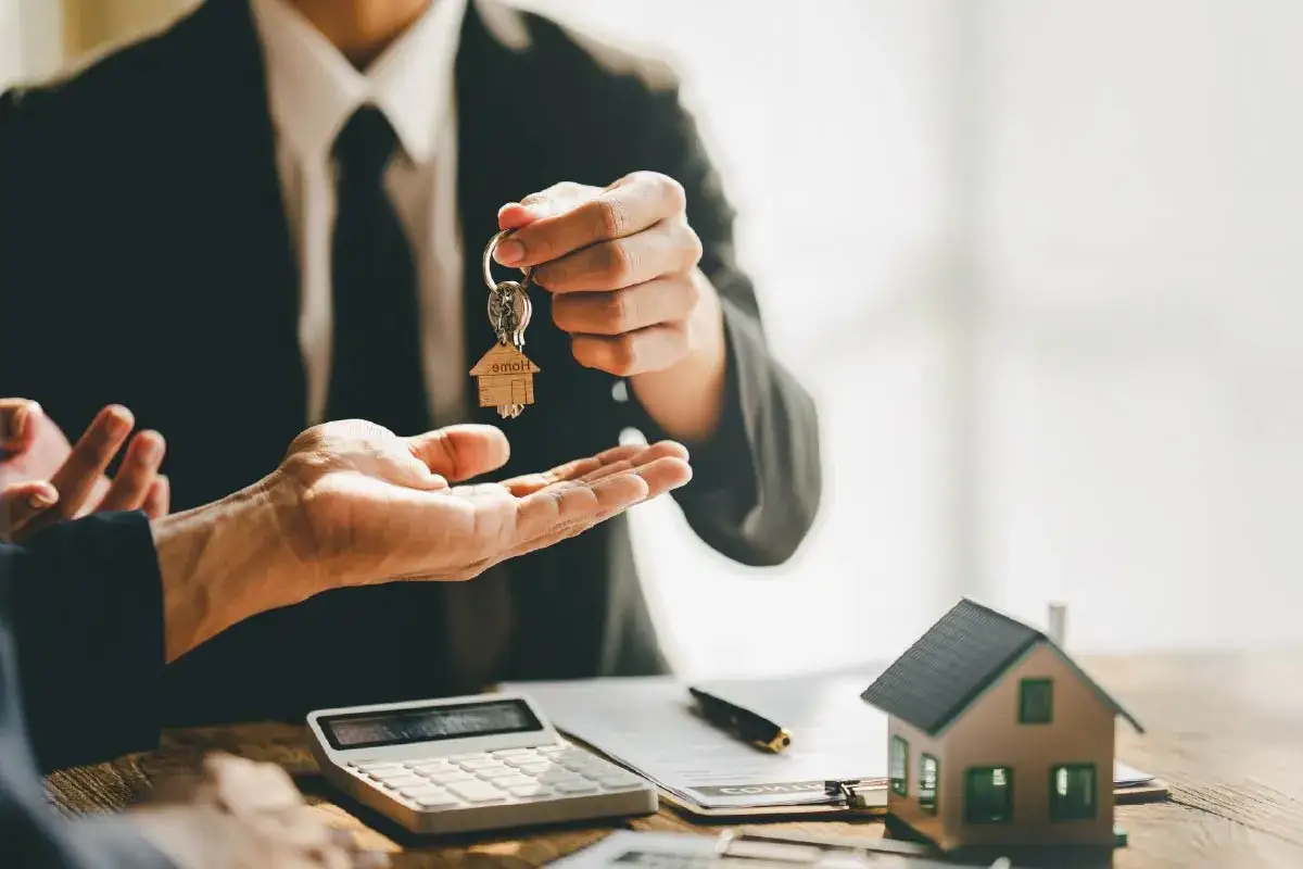 Agent remettant les clés d'une maison, symbolisant une vente à terme réussie. Une calculatrice et un contrat sont visibles.