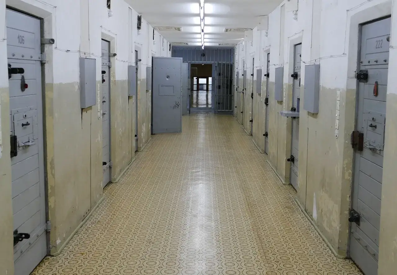 Korytarz więzienny z celami, gdzie może być orzeczona zastępcza kara pozbawienia wolności. Drzwi cel są zamknięte, a na końcu korytarza widać kraty.