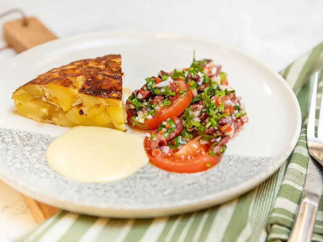 En bit spansk omelett med potatis och l&ouml;k, serverad med en tomatsallad och en klick majonn&auml;s.