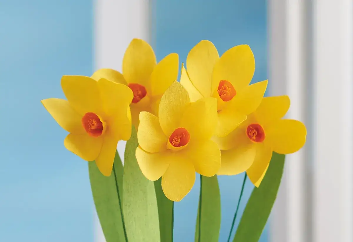 Ein Strau&szlig; selbstgebastelter gelber Narzissen mit gr&uuml;nen Bl&auml;ttern vor blauem Hintergrund. Perfekt f&uuml;r Fr&uuml;hlingsdeko.