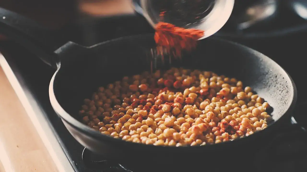 Garbanzos fritos en sartén, espolvoreando pimentón rojo para darles un toque picante y delicioso.