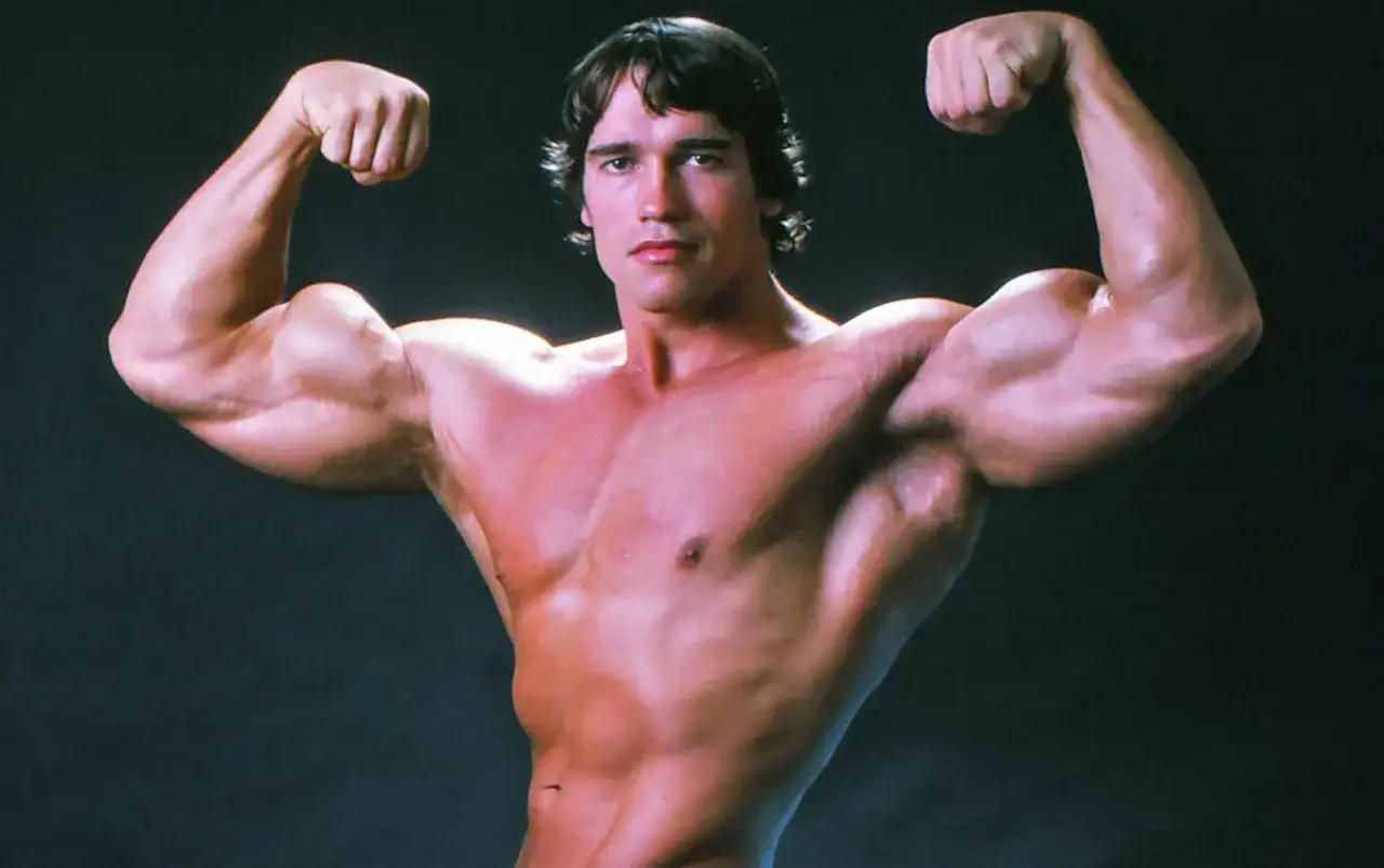 Arnold Schwarzenegger prezentuje imponującą muskulaturę. Ciekawe, ile lat ma Schwarzenegger na tym zdjęciu, gdy tak imponuje siłą.