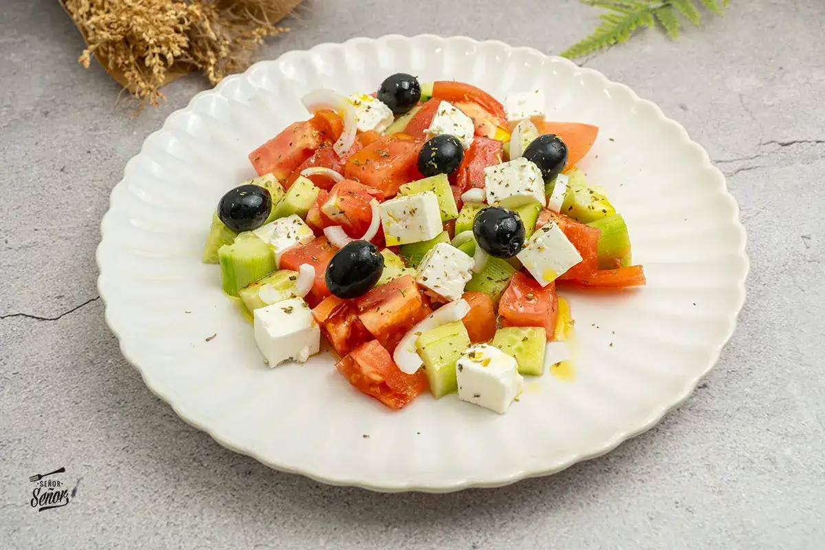 Una refrescante ensalada griega con tomates, pepinos, cebolla, aceitunas negras y cubos de queso feta, aderezada con aceite de oliva y hierbas.