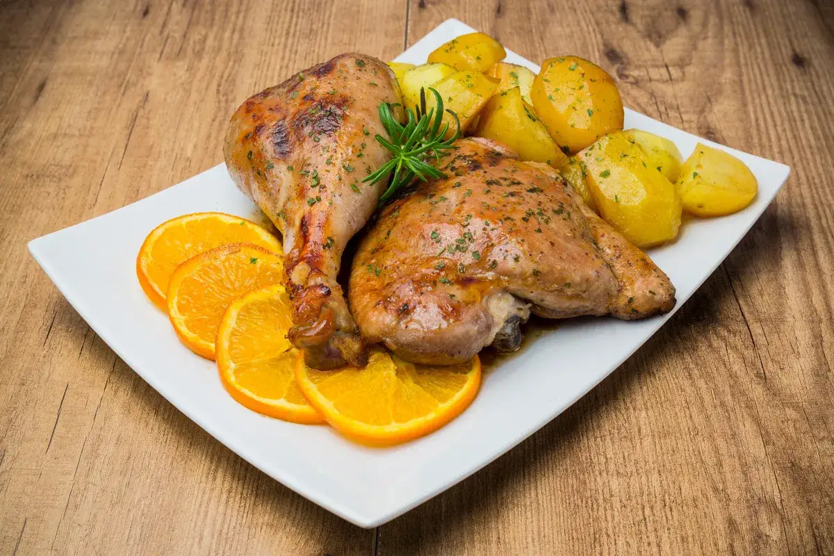 Delizioso arrosto di tacchino con patate arrosto e fette d'arancia su un piatto bianco.