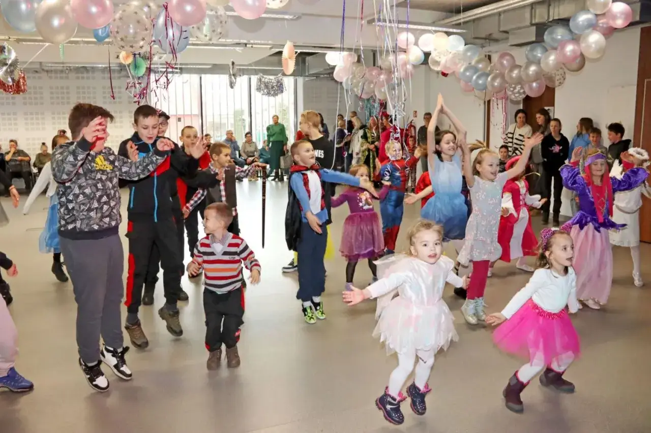 Dzieci w strojach tańczą, słychać radosne dźwięki w muzyce. Balony tworzą kolorową oprawę imprezy.