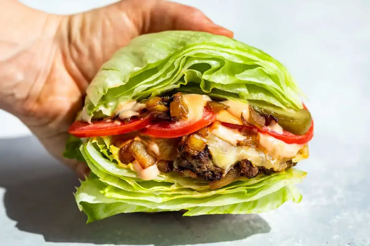 Soczysty burger owinięty w chrupiącą sałatę lodową, z pomidorem, piklami i karmelizowaną cebulką. Idealna sałata do burgera dla zdrowej alternatywy.