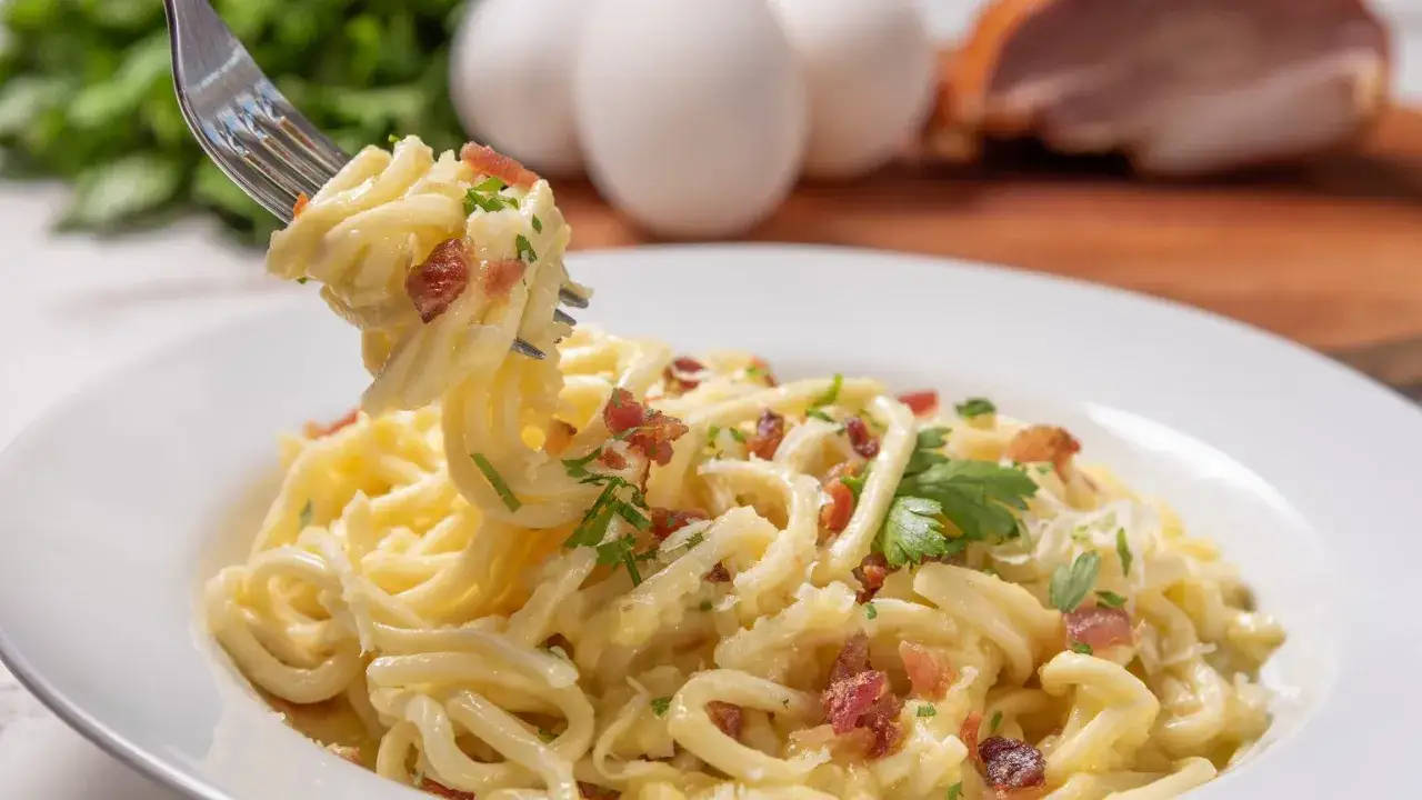 Pyszne spaghetti carbonara, jak zrobić sos carbonara bez śmietany zgodnie z włoską tradycją. Na widelcu porcja makaronu z jajkiem, guanciale i parmezanem.