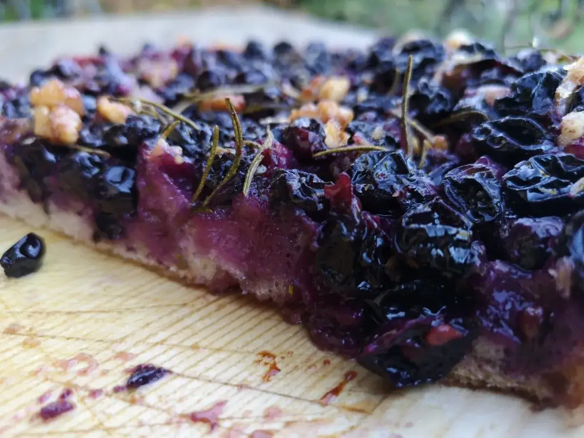 Schiacciata con l'uva succosa, rosmarino e noci su un tagliere di legno. Un morso invitante di dolcezza autunnale.