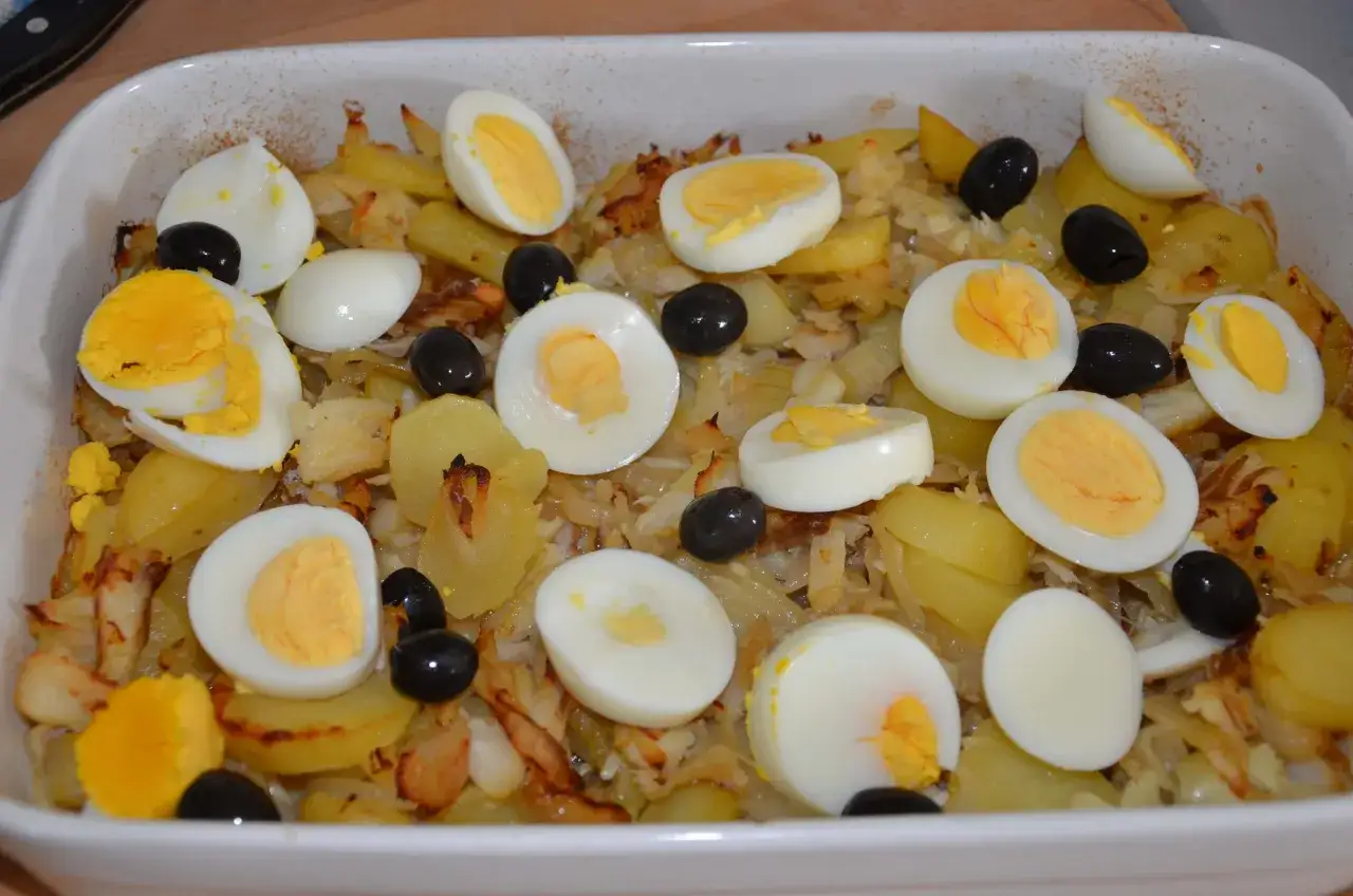 Un plat de bacalhau &agrave; bras, avec des pommes de terre, des &oelig;ufs durs coup&eacute;s et des olives noires.