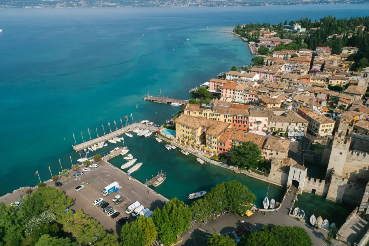 Vista aerea del **centro storico di Gardone Riviera** con il porto turistico, le case colorate e il lago.