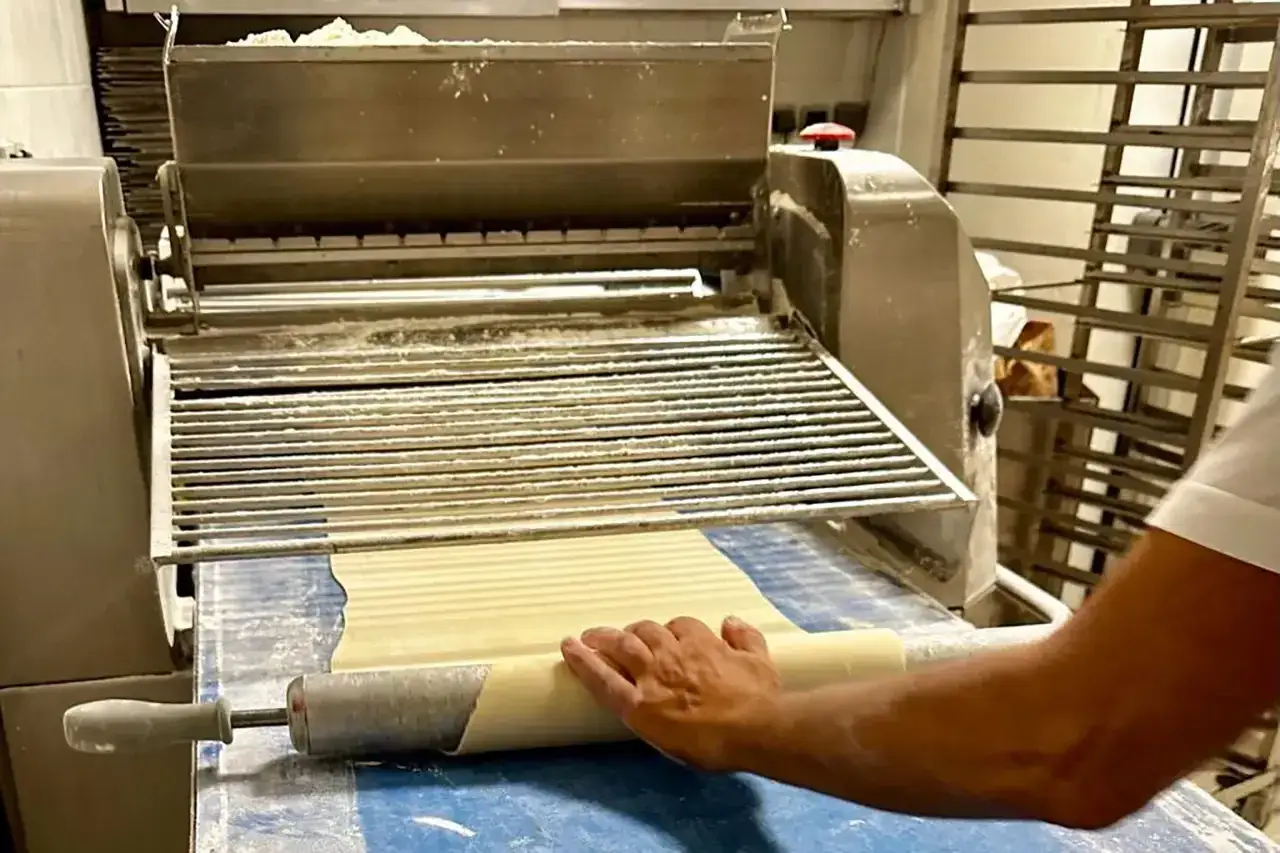 Main d'un pâtissier utilisant une machine pour étaler de la pâte. Peut-on ouvrir une boulangerie avec un CAP Pâtissier ? Oui, c'est le début d'une belle aventure !
