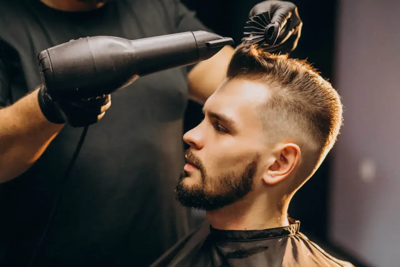 Un homme se fait s&eacute;cher les cheveux par un coiffeur, arborant une barbe stylis&eacute;e avec un d&eacute;grad&eacute; barbe &agrave; blanc.