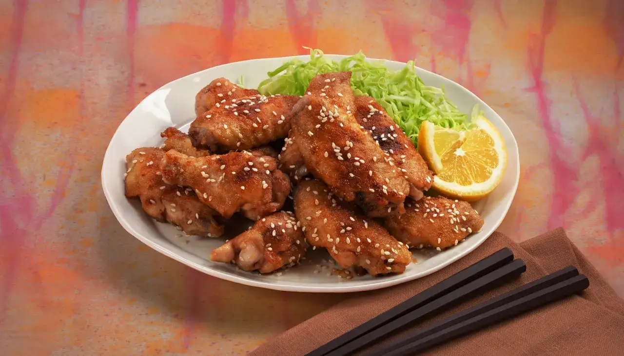 A plate of glistening Nagoya style chicken wings, sprinkled with sesame seeds, served with shredded cabbage and a lemon wedge.