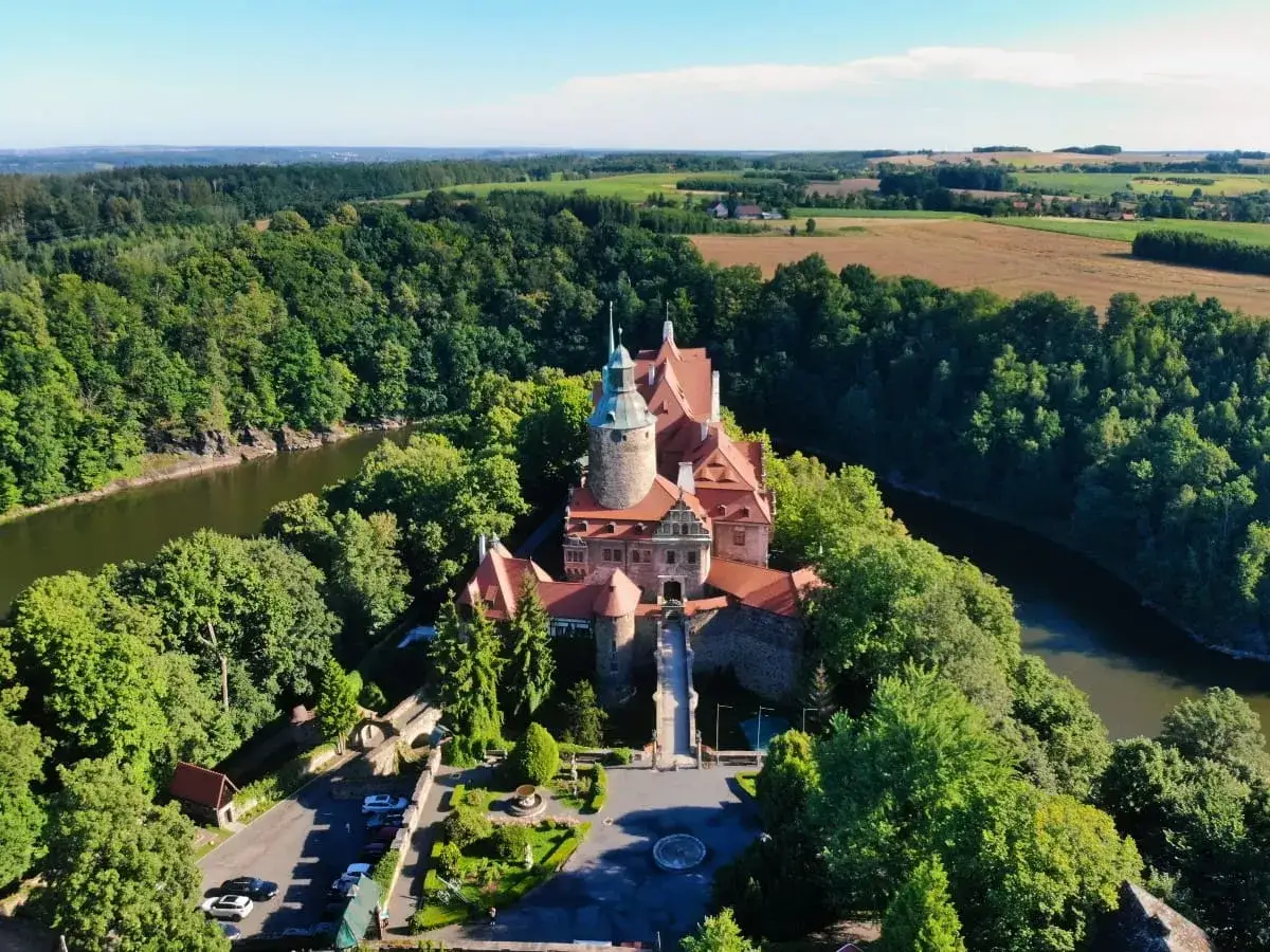 Zamek Czocha, malowniczo położony nad rzeką, otoczony bujną zielenią.