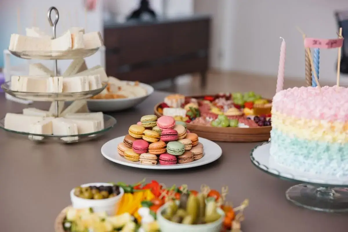Mesa de baby shower con pastel de arco&iacute;ris, s&aacute;ndwiches, macarons y tabla de quesos. &iexcl;Comida deliciosa para celebrar!