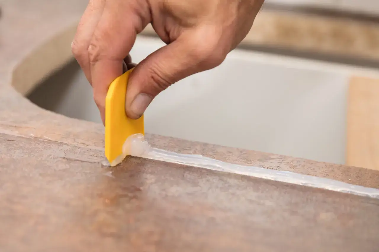 Hand glättet Silikonfuge mit gelbem Werkzeug. Wichtig: wie lange muss silikon trocknen dusche, bevor sie wieder genutzt werden kann.