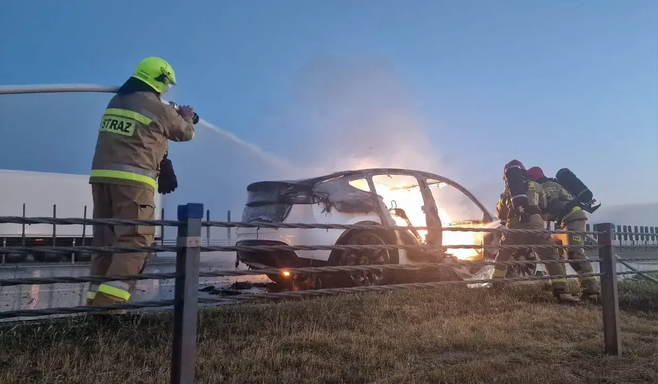 Strażacy walczą z płonącym samochodem. To prawdziwy domowy survival, gdy trzeba gasić pożar na poboczu drogi.