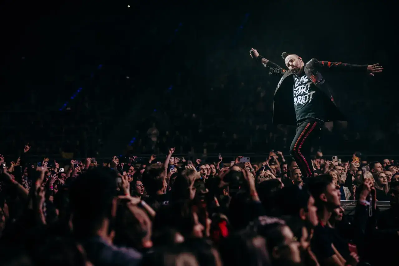 Wokalista Three Days Grace Polska na koncercie, z tłumem fanów nagrywających telefonami.
