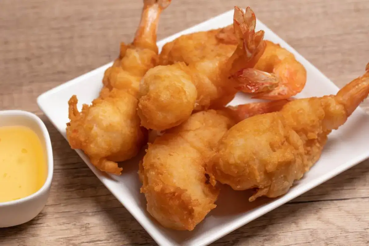 Gambas a la gabardina doradas y crujientes, servidas en plato blanco junto a un cuenco con salsa.