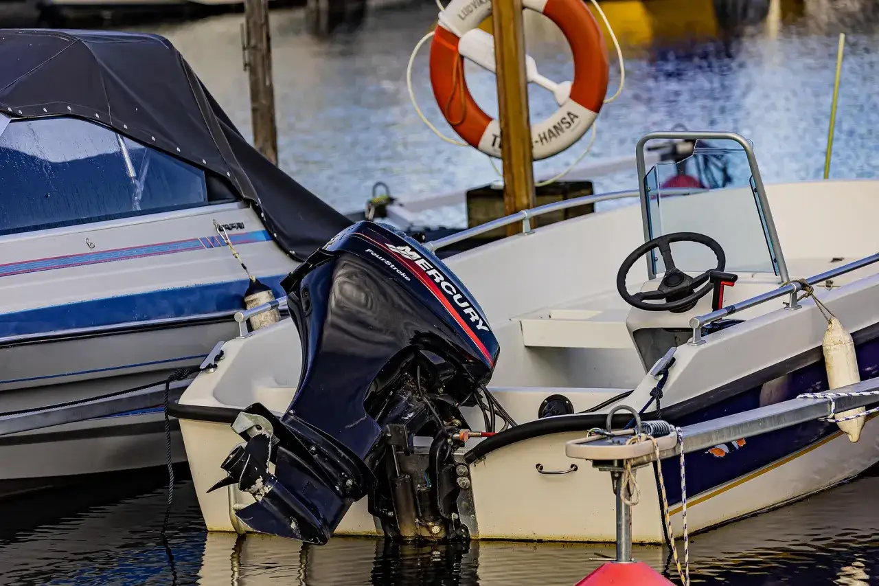 Moteur Mercury hors-bord, probablement en panne, sur un bateau blanc amarré. Une bouée de sauvetage orange est visible.
