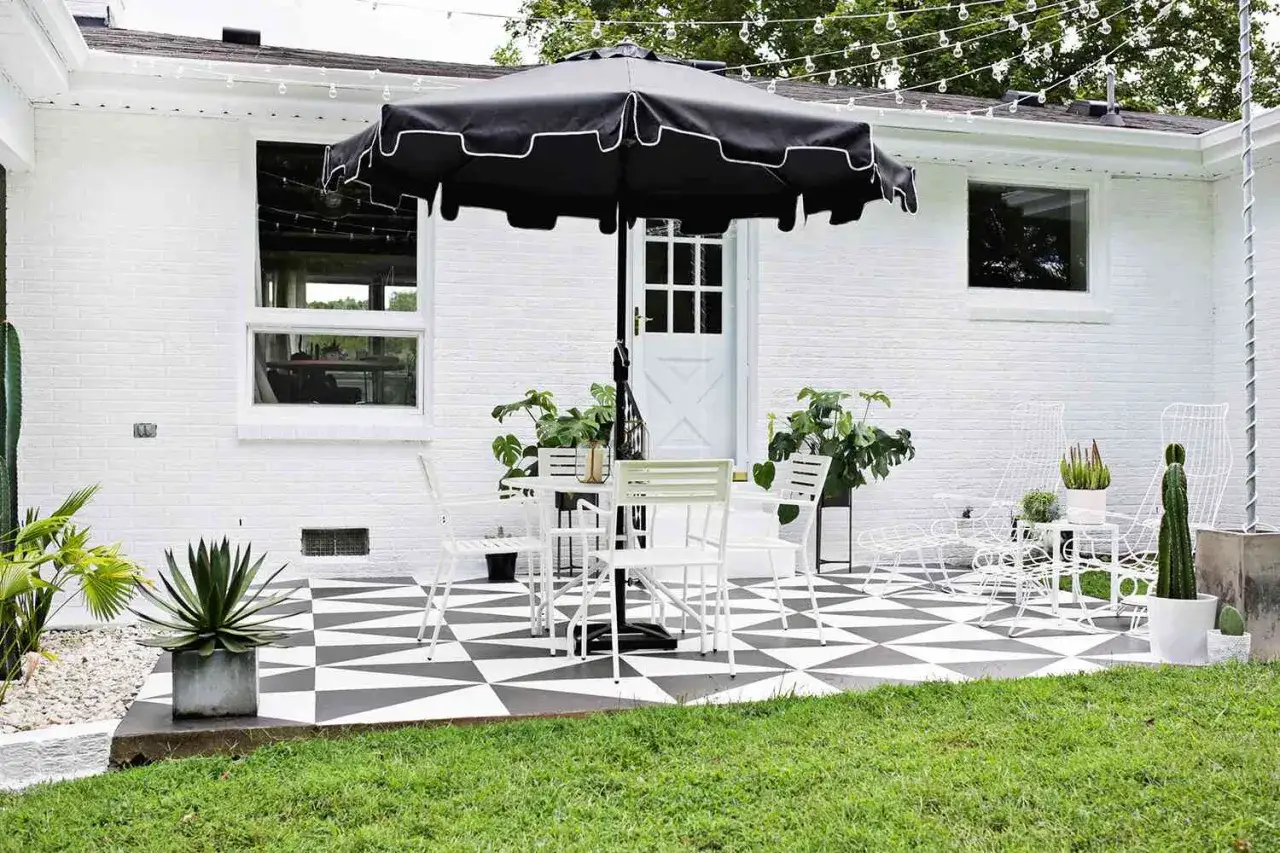 Terraza con suelo de baldosas pintadas en blanco y negro, mesa, sillas y sombrilla. Un espacio ideal para disfrutar al aire libre.