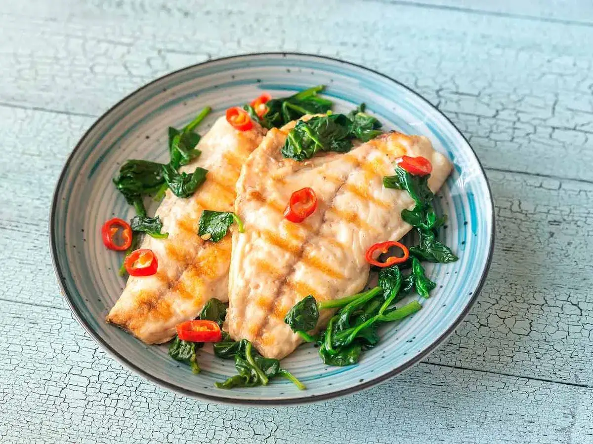 Dos filetes de pescado a la plancha con espinacas y rodajas de chile rojo. Un plato saludable de verduras a la plancha.