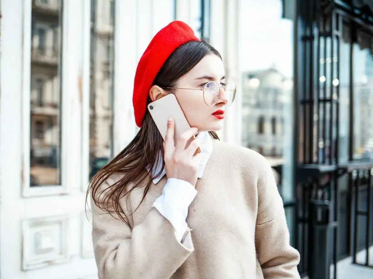 Elegancka kobieta w czerwonym beretcie rozmawia przez telefon. Pokazuje, jak założyć beret, by wyglądać stylowo.