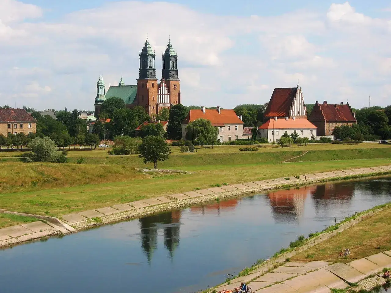 Widok na Ostrów Tumski w Poznaniu z katedrą i innymi zabytkowymi budynkami nad rzeką Wartą.