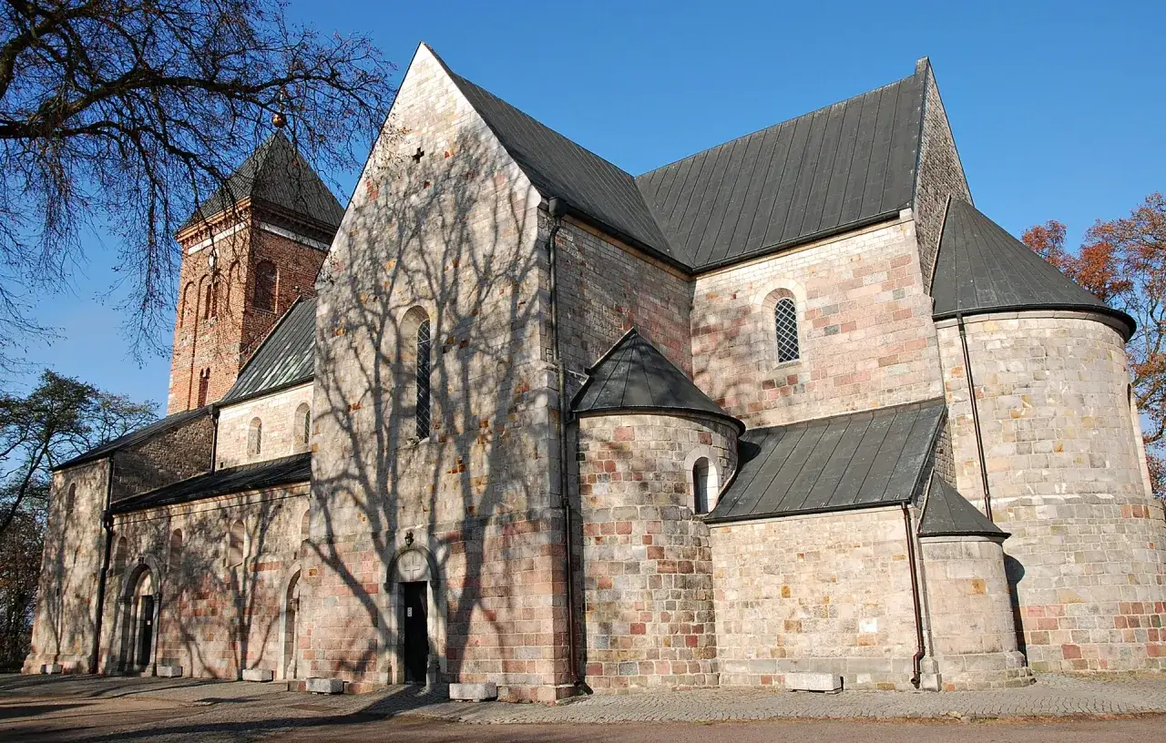 Kamienna budowla z ceglaną wieżą, przykład sztuki średniowiecza, z cieniami drzew na ścianach.