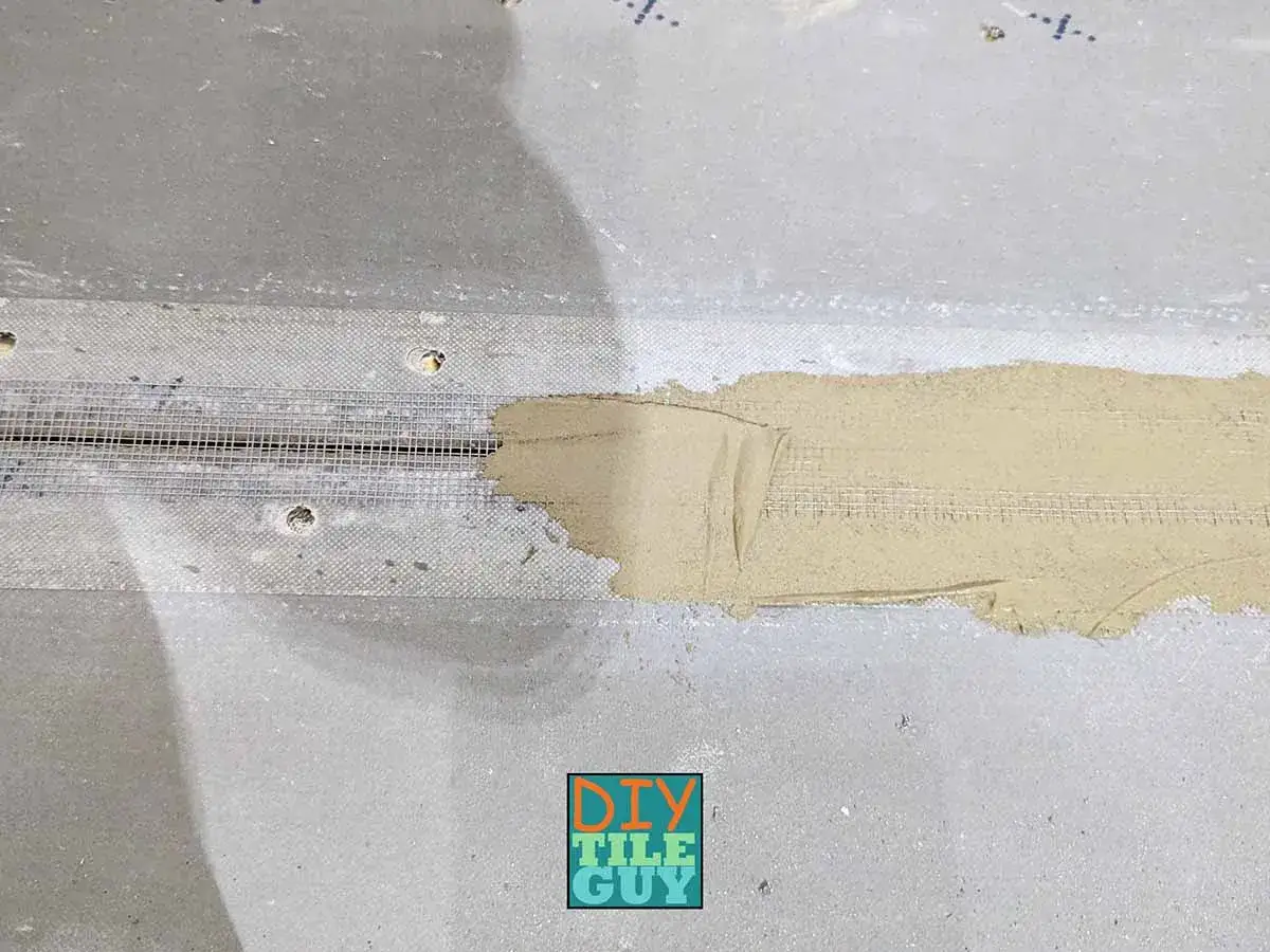Mesh tape and thin-set mortar are applied over cement board seams, preparing the surface for tile.