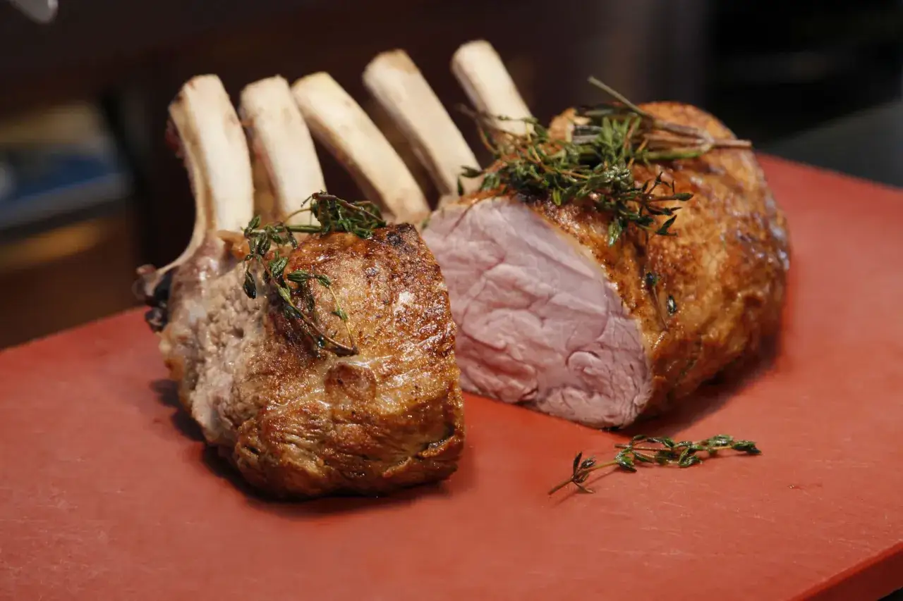 Ein saftiger Semerrolle Kalb Braten, mit Kräutern garniert, liegt auf einem roten Schneidebrett.
