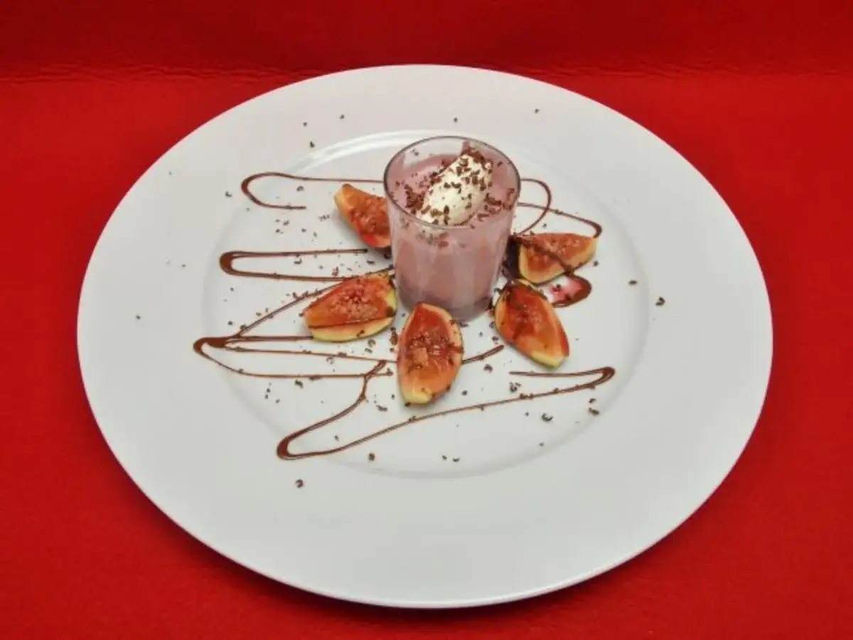Ein Glas rotweincreme selbstgemacht, garniert mit Sahne und Schokostreuseln, daneben Feigenspalten auf einem Teller mit Schokoladensauce.