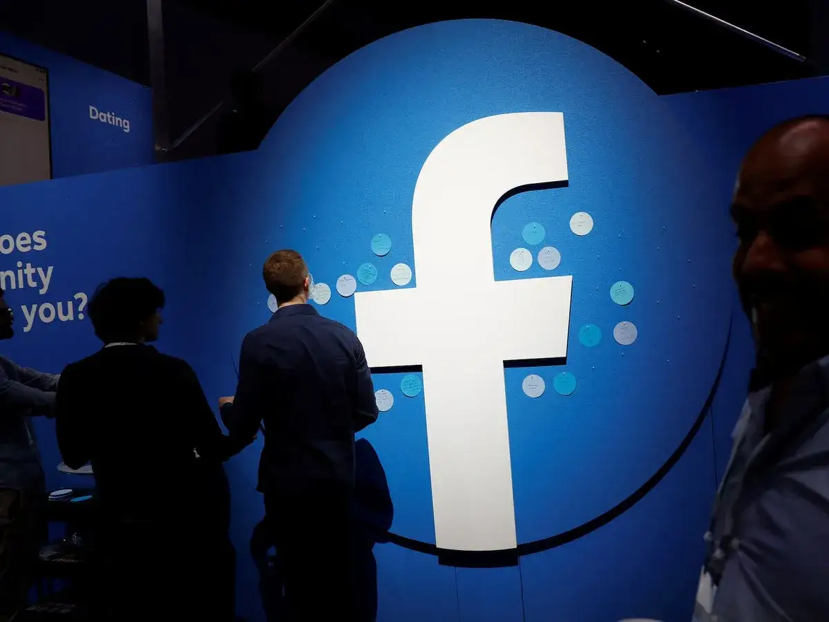 Ludzie przyglądają się dużemu logo Facebooka. Może to być inspiracja, jak usunąć relacje z FB, gdy już nie są potrzebne.