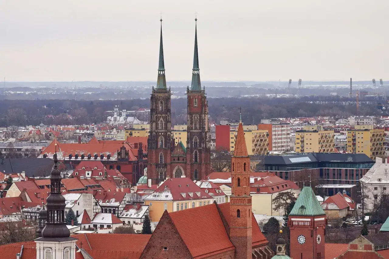 Dwie wieże kościoła garnizonowego we Wrocławiu g&oacute;rują nad miastem z czerwonymi dachami.