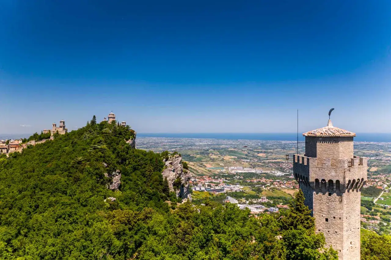 Torri medievali su un monte verdeggiante, con una vista panoramica sul mare e sulla città. Un'immagine che evoca la storia di San Marino.