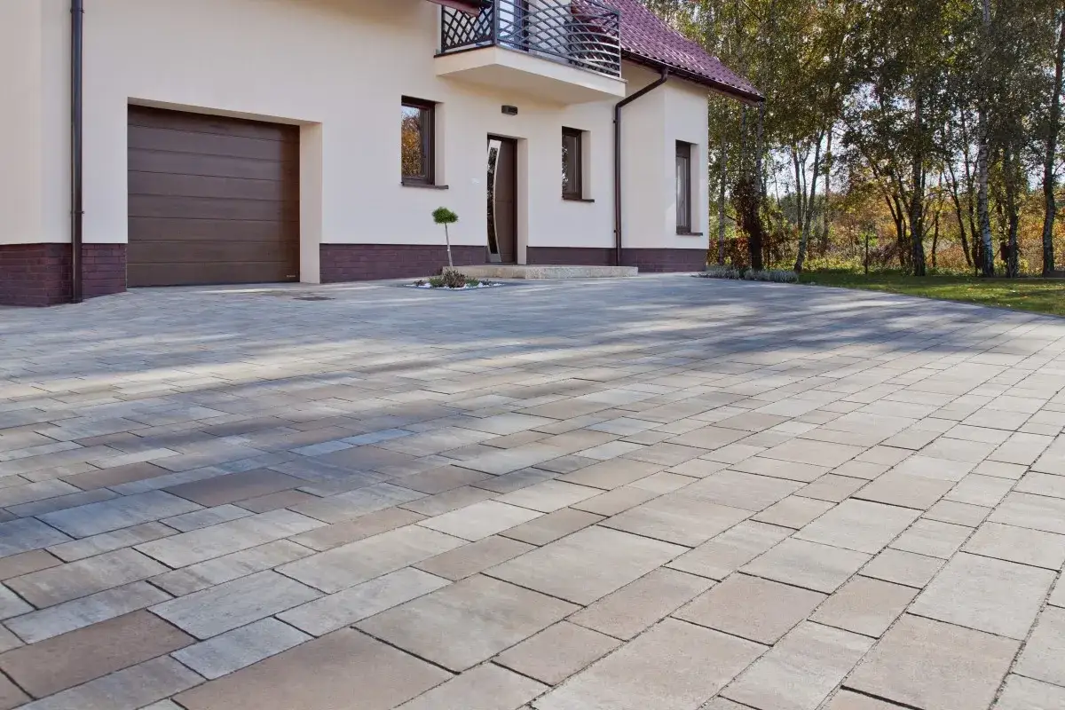 Nowy podjazd z behatonu przed domem, z garażem i wejściem, otoczony zielenią.