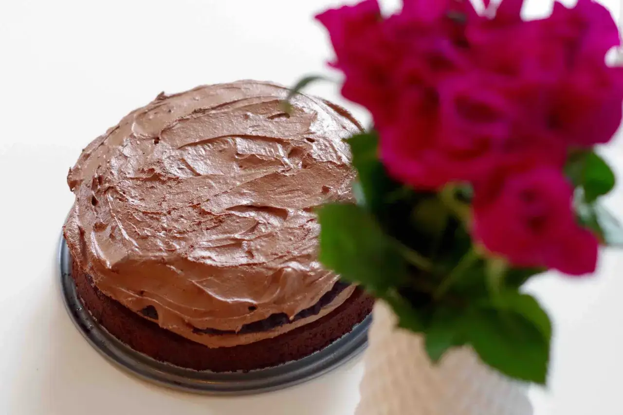 En läcker vegansk tårta med chokladfrosting, dekorerad med rosa blommor.