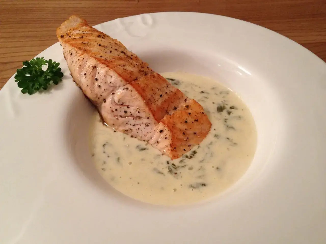 Un délicieux pavé de saumon poêlé repose dans une onctueuse sauce oseille, garni d'une touche de persil frais.